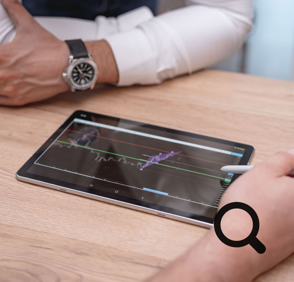 Close-up of hands using a digital tablet with trading charts on a wooden desk.